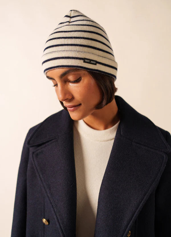 Person in marineblauem Mantel und SAINT JAMES Bonnet Marée, die vor einem schlichten hellen Hintergrund nach unten schaut.