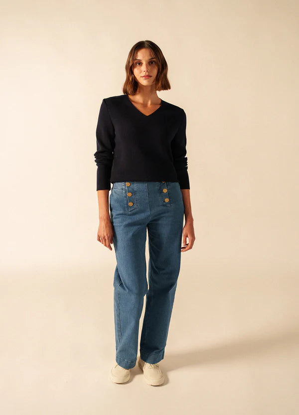Frau in einem Atelier. Sie trägt den SAINT JAMES Brehat navy V-Ausschnitt Damen Strickpullover, blaue Jeans und weiße Schuhe.
