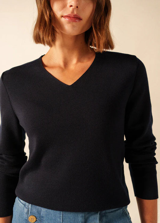 Frau in einem schwarzen SAINT JAMES Brehat Strickpullover mit V-Ausschnitt und blauen Jeans, dargestellt von den Schultern bis zur Taille.