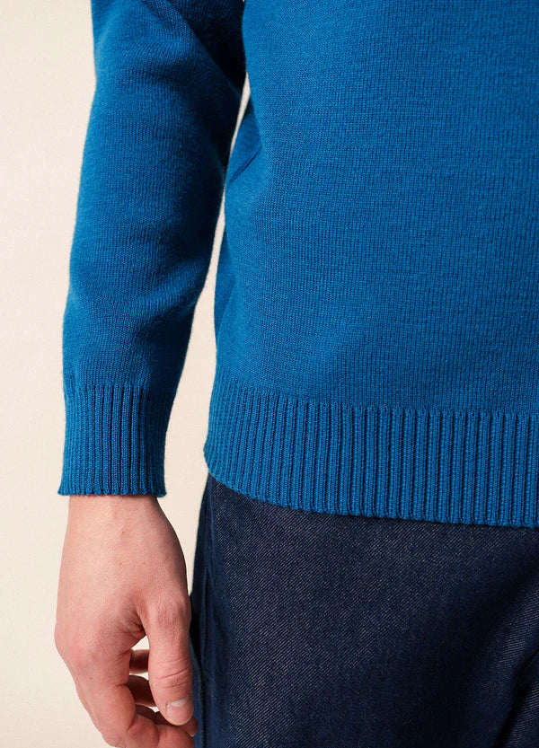 Eine Person in einem blauen SAINT JAMES Cancale Pullover und dunklen Jeans, die linke Hand entspannt an der Seite.