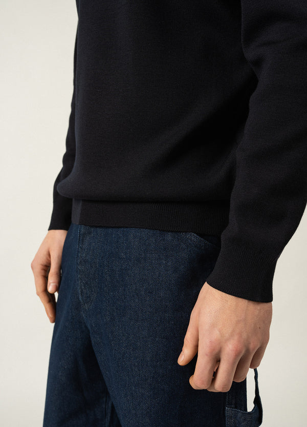 Eine Person trägt den Cruiser Wollpullover von SAINT JAMES und eine blaue Jeans, sichtbar von Taille bis Mitte Oberschenkel.