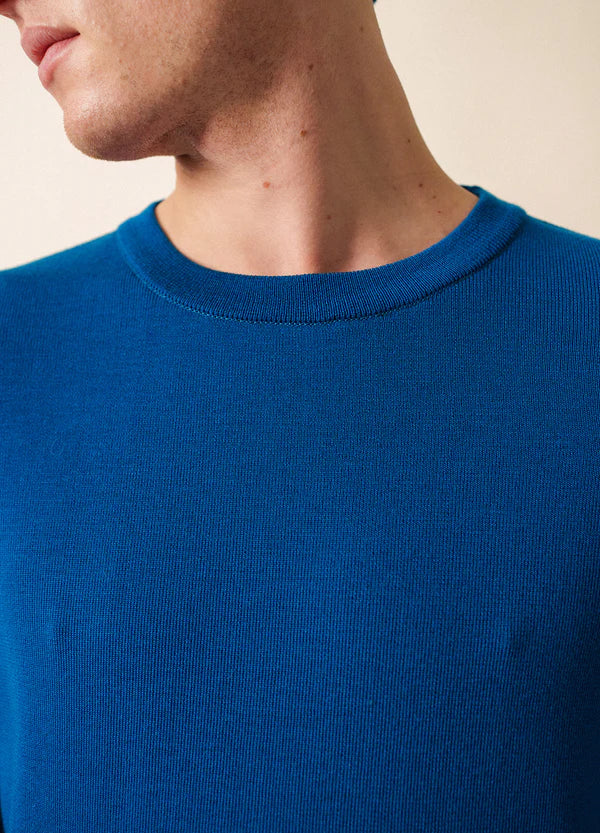 Nahaufnahme einer Person in der blauen SAINT JAMES Cruiser Crewneck aus Wolle, die Hals und Gesicht vor einem neutralen Hintergrund zeigt.