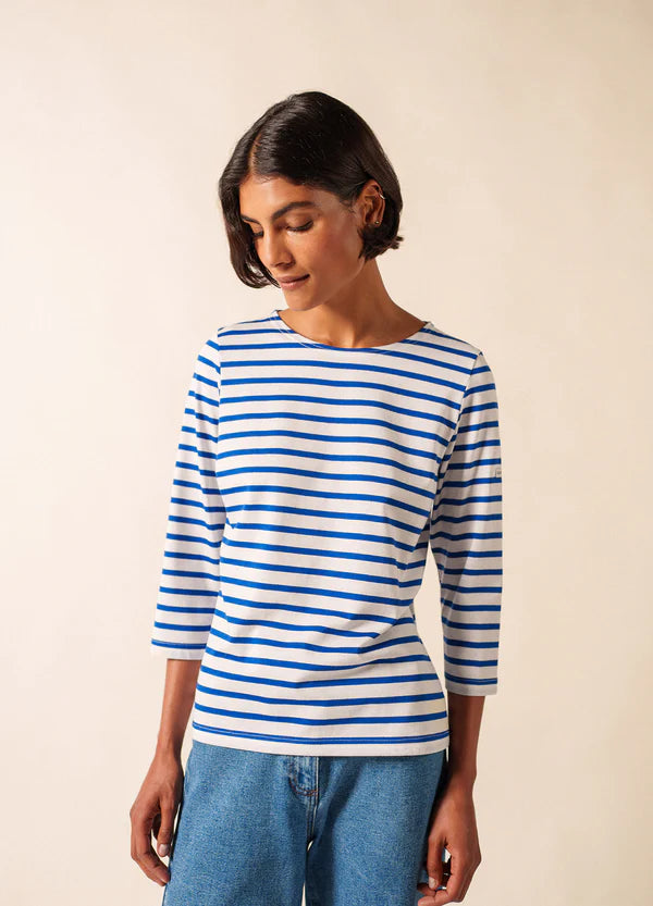 Person, die eine SAINT JAMES Galathee marinière und Blue Jeans trägt und vor einem neutralen Hintergrund nach unten schaut.