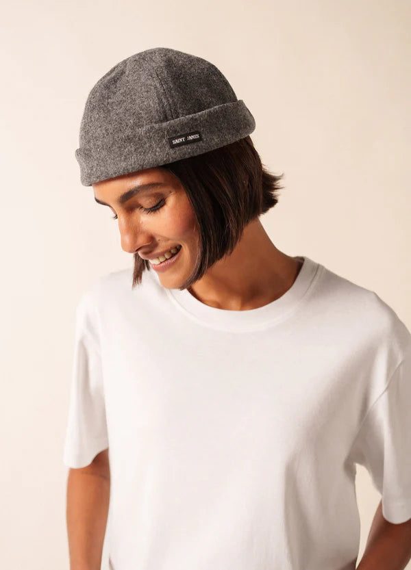 Person, die einen grauen SAINT JAMES Marin Miki-Hut und ein weißes T-Shirt trägt, lächelt und blickt auf einen schlichten Hintergrund.