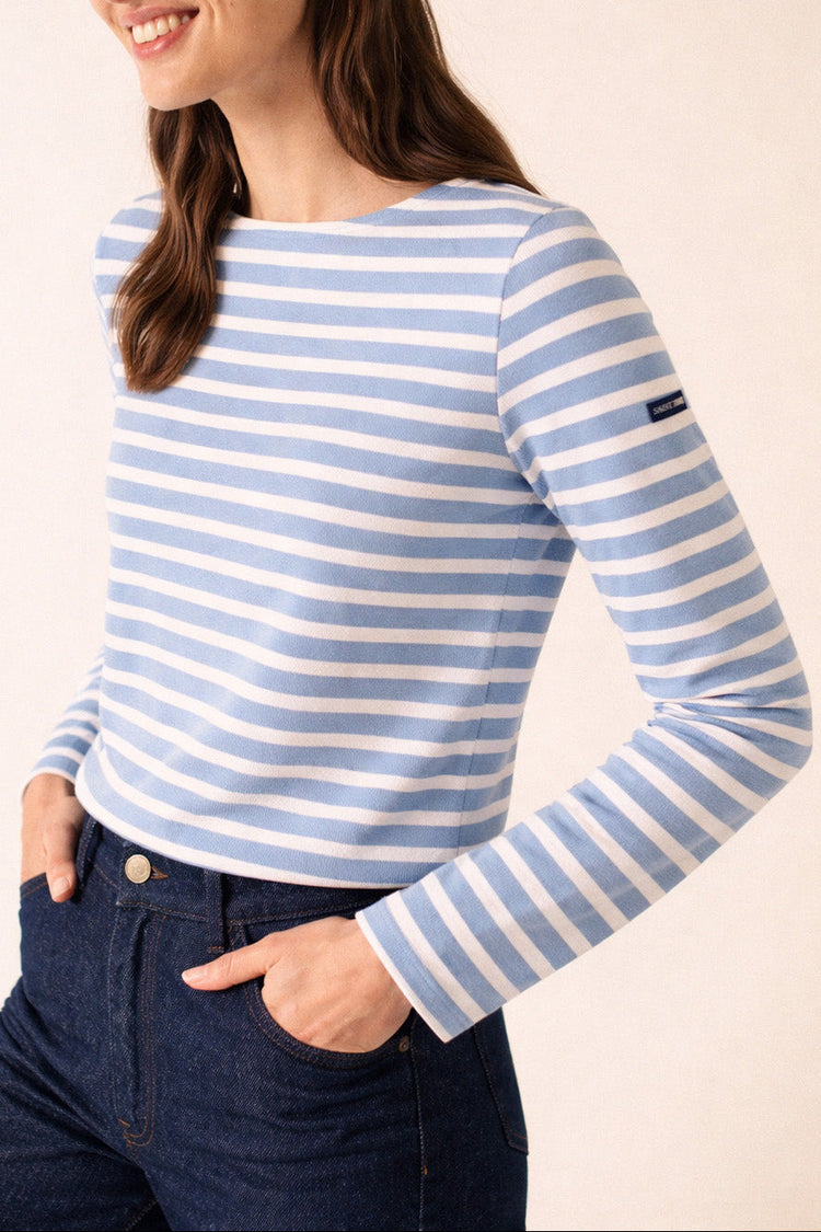 Frau in einem hellblau-weiß gestreiften Meridame-Hemd von SAINT JAMES, trägt dunkle Jeans und lächelt.