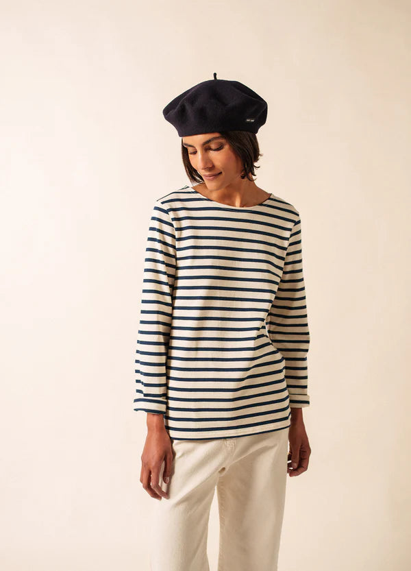 Eine Person in einem Meridien Moderne von SAINT JAMES und einer marineblauen Baskenmütze steht vor einem schlichten beigen Hintergrund.