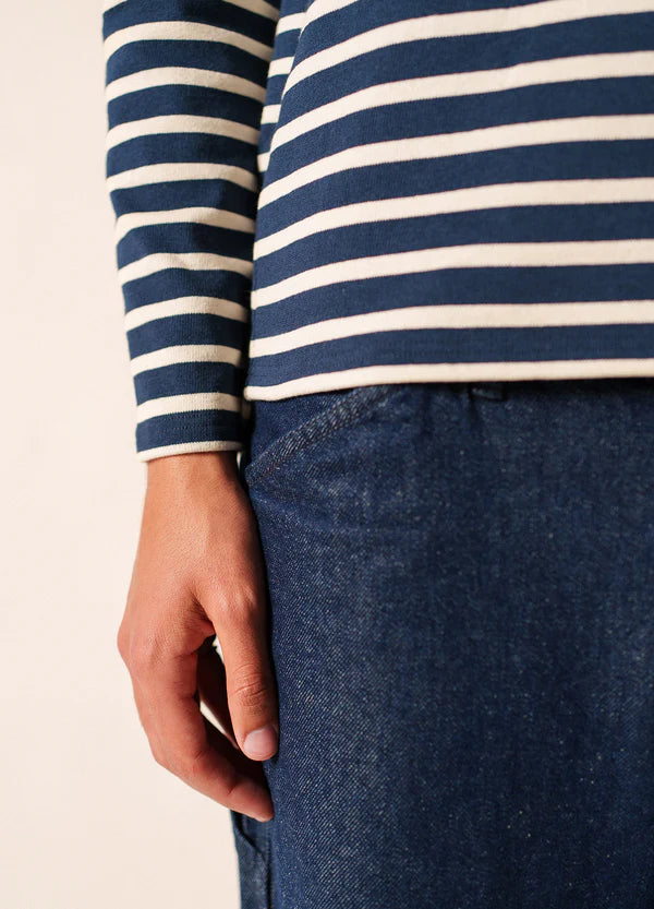 Jemand in einem marineblau-weiß gestreiften SAINT JAMES Meridien Moderne Hemd und blauen Jeans, die linke Hand an der Seite.