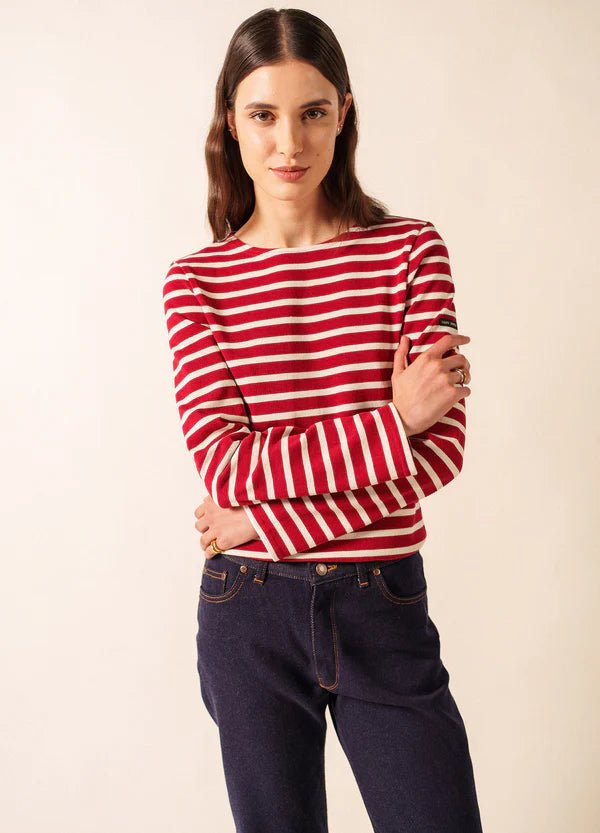 Frau mit langen braunen Haaren trägt das SAINT JAMES Meridien Moderne marinière Oberteil und dunkle Jeans, Arme verschränkt.