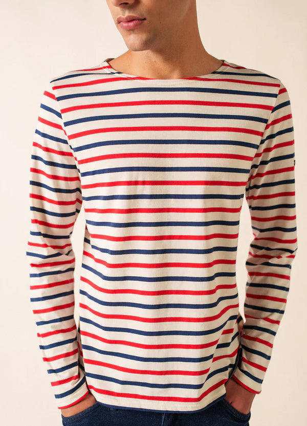 Jemand trägt das SAINT JAMES Minquier Tri Unisex-Langarmhemd in Weiß mit roten und marineblauen Streifen, die Hände in den Taschen.