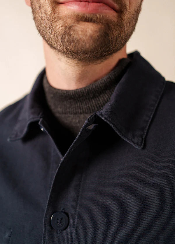 Nahaufnahme eines Mannes, der das marineblaue SAINT JAMES Sirocco Hemd mit Knopfleiste über einem dunkelgrauen Rollkragenpullover trägt.