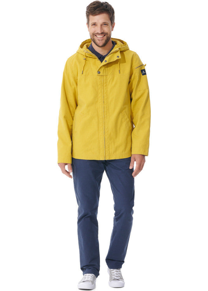 Ein lächelnder Mann in einer gelben MOUSQUETON Baden-Jacke, einer blauen Hose und grauen Turnschuhen steht vor einem weißen Hintergrund.