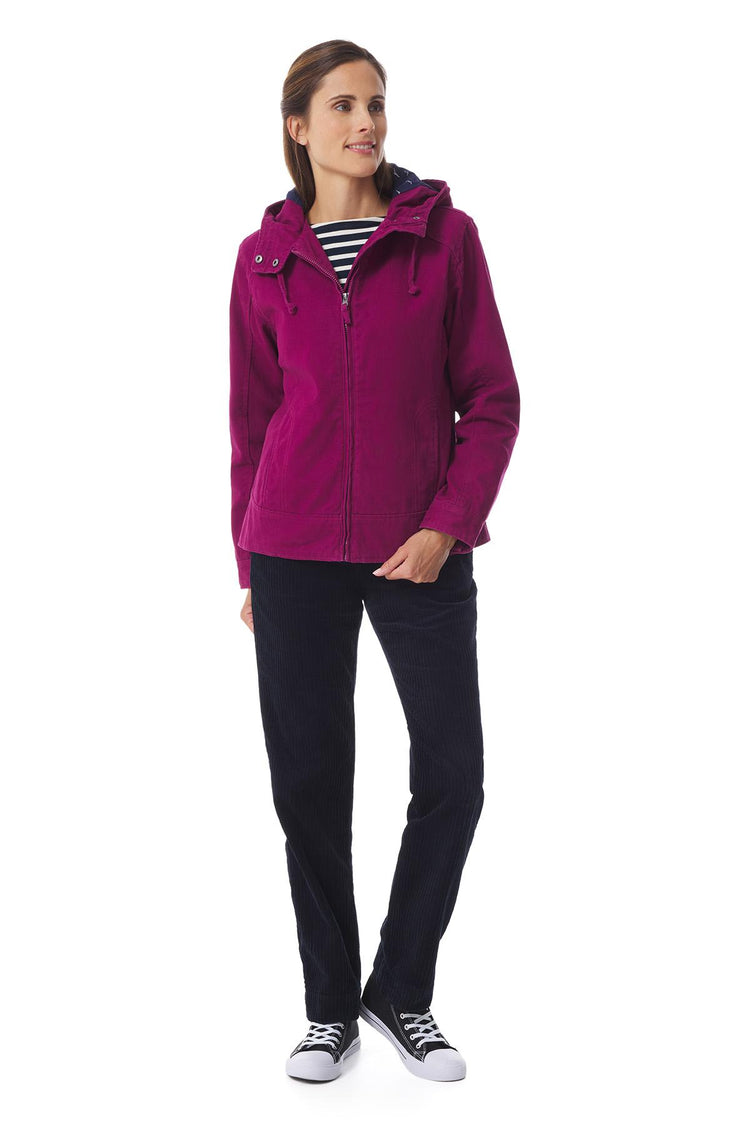 Frau mit der magentafarbenen Jacke MOUSQUETON Fiona, gestreiftem Hemd, schwarzer Hose und Turnschuhen auf weißem Hintergrund.