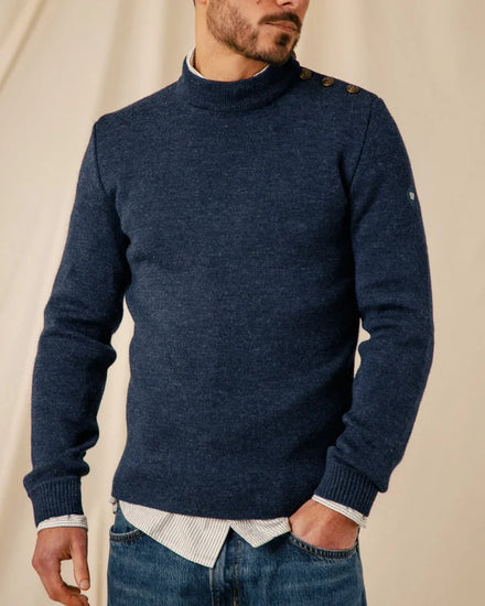 Ein Mann trägt einen marineblauen Pullover von ROYAL MER Adrian mit Schulterknöpfen über einem gestreiften Hemd und Jeans.