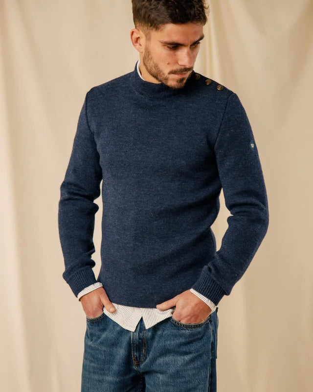 Mann in einem Matrosenpullover „Adrian“ aus Schurwolle von ROYAL MER, weißem Hemd und blauen Jeans, der nach unten schaut.