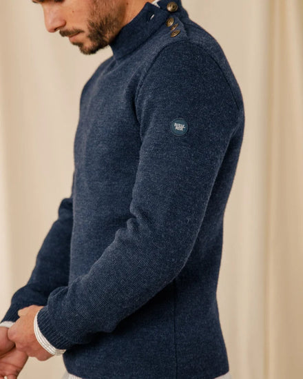 Ein Mann trägt einen marineblauen Pullover aus Schurwolle von ROYAL MER Adrian mit geknöpftem Kragen und blickt vor einem neutralen Hintergrund nach unten.