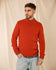 Ein Mann in einem „ROYAL MER Adrian“-Pullover mit Knöpfen an den Schultern steht vor einem beigen Hintergrund und blickt zur Seite.