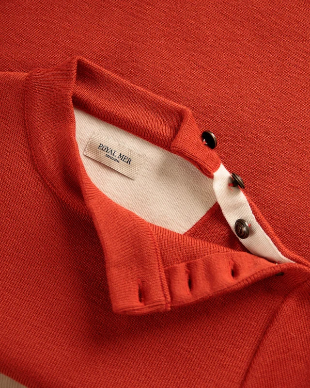 Nahaufnahme des orangefarbenen Strickhemds „Adrian“ von ROYAL MER mit Kragen, Knöpfen und Etikett, inspiriert vom Matrosenpullover-Stil.