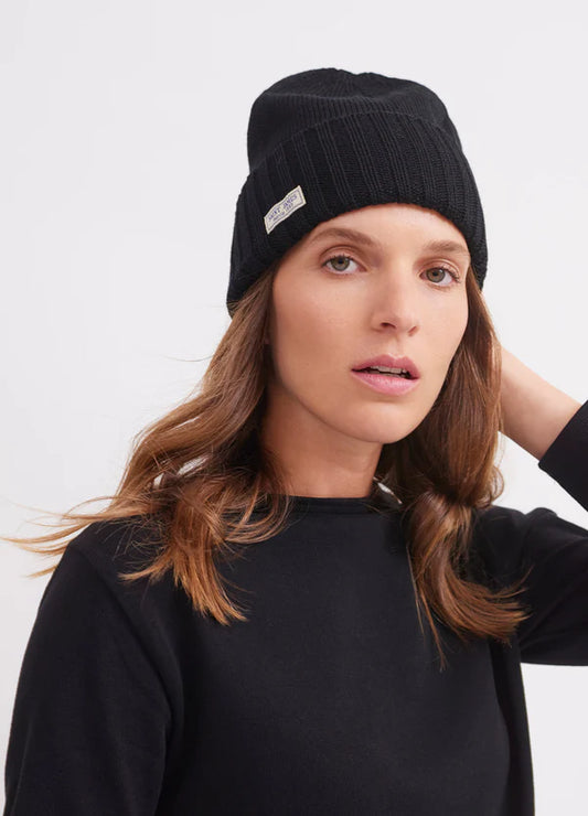 Eine Frau mit gewelltem braunem Haar trägt einen schwarzen SAINT JAMES-Barbarenhut und ein Oberteil und schaut neutral in die Kamera.