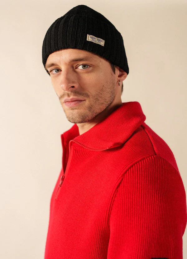 Mann in schwarzer Barbaresque von SAINT JAMES und leuchtend rotem Pullover mit Reißverschluss, schaut ernst in die Kamera.
