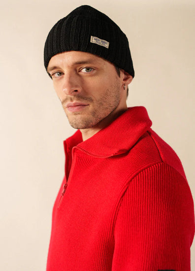 Mann in schwarzer Barbaresque von SAINT JAMES und leuchtend rotem Pullover mit Reißverschluss, schaut ernst in die Kamera.
