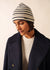 Person mit SAINT JAMES Bonnet De Quart, cremefarbenem Pullover und marineblauem Mantel, die vor einem neutralen Hintergrund nach unten schaut.