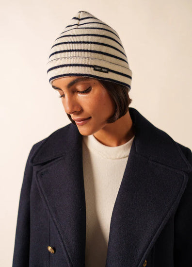 Person in marineblauem Mantel und SAINT JAMES Bonnet Marée, die vor einem schlichten hellen Hintergrund nach unten schaut.