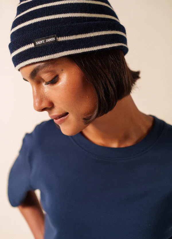 Person in einem marineblauen SAINT JAMES Bonnet De Quart und einem marineblauen Hemd, die mit neutraler Miene nach unten schaut.