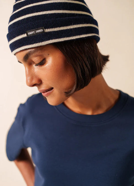 Person in einem marineblauen SAINT JAMES Bonnet De Quart und einem marineblauen Hemd, die mit neutraler Miene nach unten schaut.