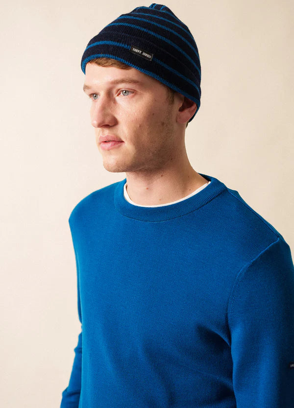 Mann in blauem Pullover und SAINT JAMES Bonnet De Quart blickt vor einem schlichten, hellen Hintergrund zur Seite.