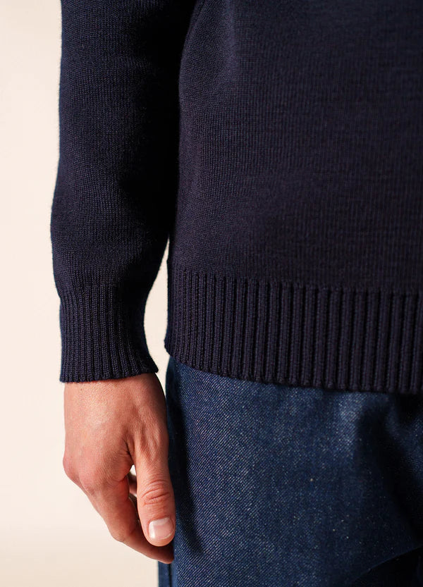 Nahaufnahme einer linken Hand in blauer Jeans und marineblauem Pullover von SAINT JAMES Cancale, Wollsaum sichtbar.