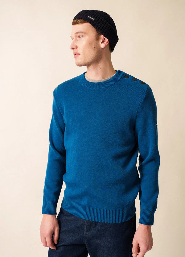 Mann in einem SAINT JAMES Cancale Matrosenpullover, Blue Jeans und schwarzer Strickmütze, der zur Seite schaut.