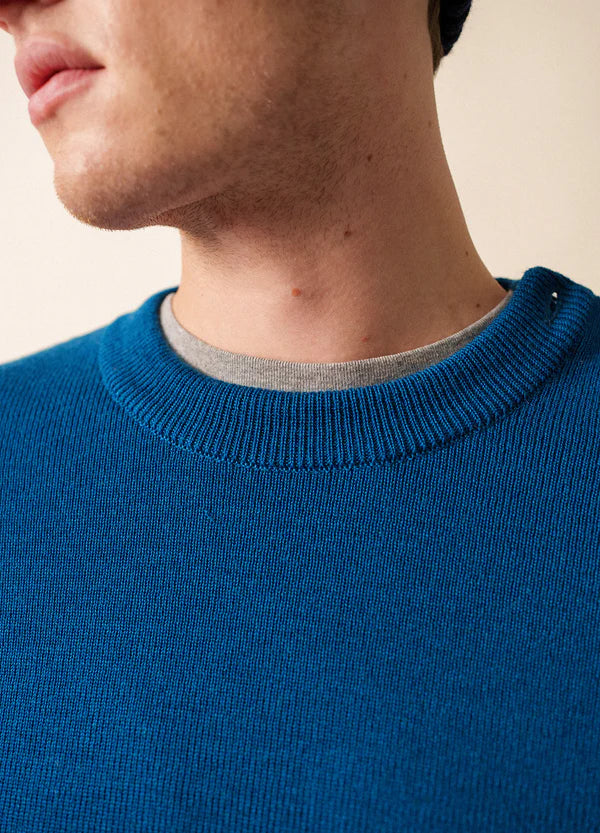 Nahaufnahme einer Person, die den blauen Matrosenpullover SAINT JAMES Cancale über einem grauen Hemd trägt, mit Blick auf Hals und Kinn.