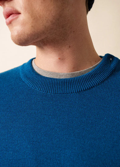 Nahaufnahme einer Person, die den blauen Matrosenpullover SAINT JAMES Cancale über einem grauen Hemd trägt, mit Blick auf Hals und Kinn.