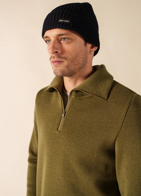 Mann in SAINT JAMES Canot Pullover mit olivfarbenem Reißverschluss und schwarzer Wollmütze, Blick zur Seite vor einem neutralen Hintergrund.