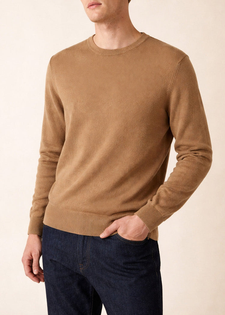 Ein Mann in einem SAINT JAMES Cruiser Wollpullover mit Rundhalsausschnitt und dunkelblauen Jeans steht mit einer Hand in der Tasche.