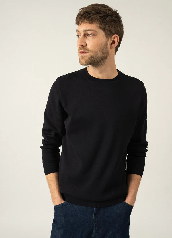 Mann mit kurzen braunen Haaren und Bart, bekleidet mit einem SAINT JAMES Cruiser-Pullover und blauen Jeans, Blick nach links.