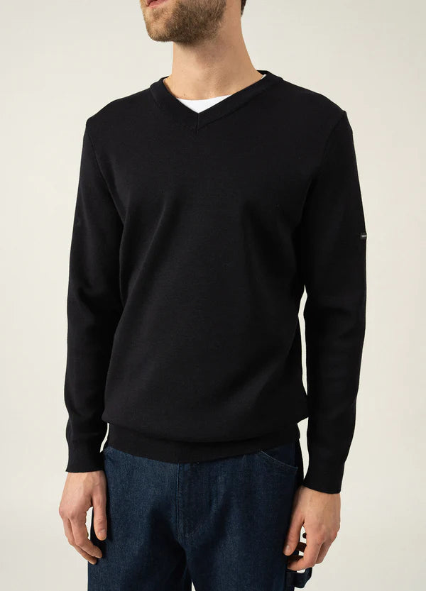 Mann im SAINT JAMES Cuirassé Feinstrickpullover mit V-Ausschnitt, weißem Hemd und Jeans vor hellem Hintergrund.