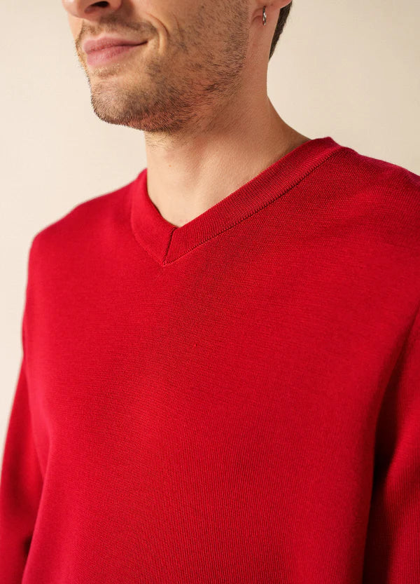 Mann in einem leuchtend roten SAINT JAMES Cuirassé Pullover mit V-Ausschnitt, lächelnd, von den Schultern aufwärts vor einem neutralen Hintergrund dargestellt.