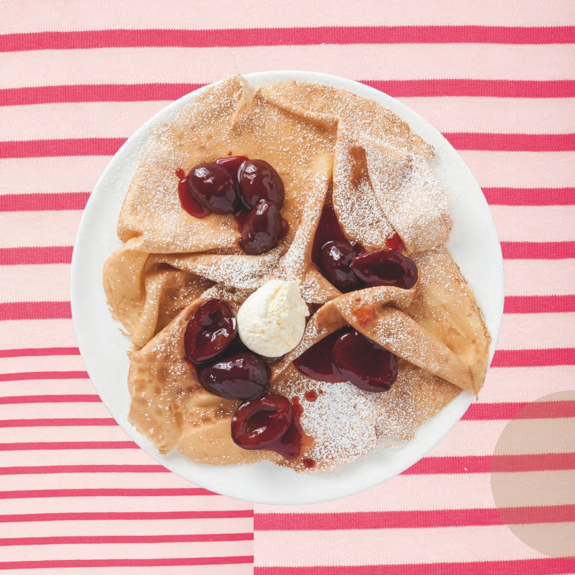 Crêpes et Galettes "c'est bon !" von Divers, belegt mit Kirschsauce, Puderzucker und Butter auf einem rosa gestreiften Tuch.