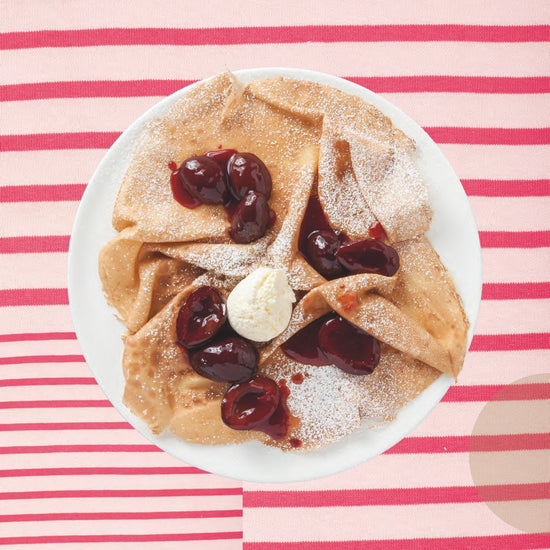 Crêpes et Galettes "c'est bon !" von Divers, belegt mit Kirschsauce, Puderzucker und Butter auf einem rosa gestreiften Tuch.