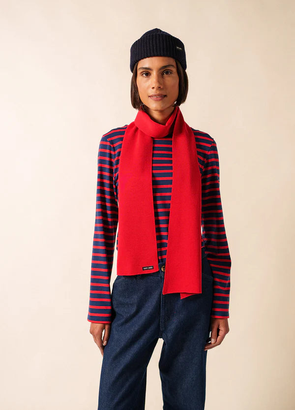 Frau mit marineblauer Mütze und geripptem Longsleeve von SAINT JAMES Duguay, mit rotem Schal, steht vor einem beigen Hintergrund.