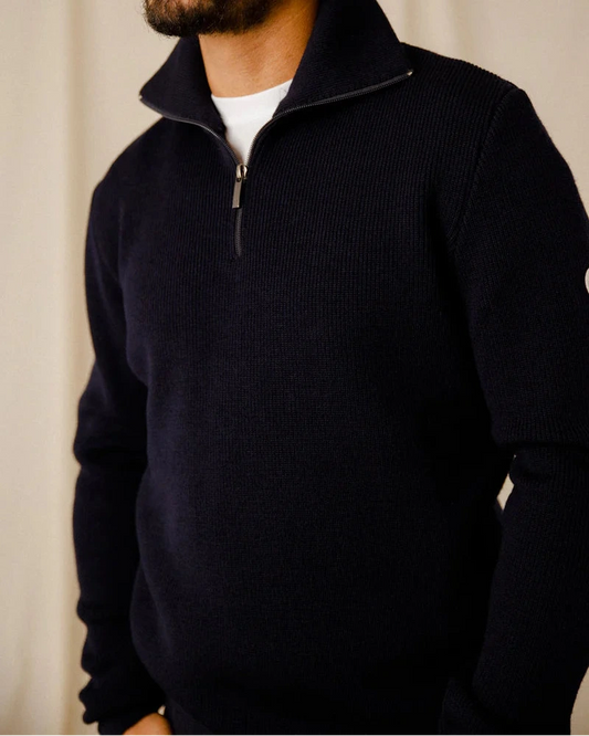 Mann in einem dunklen ROYAL MER Etrelles Pullover mit Reißverschluss über einem weißen Hemd, steht mit den Händen in den Taschen.