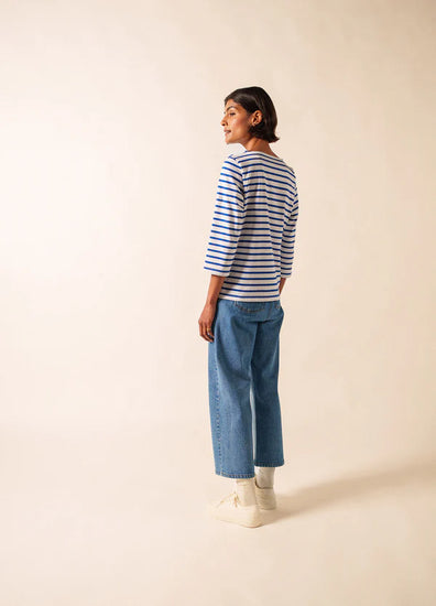 Frau, die das SAINT JAMES Galathee marinière und Blue Jeans trägt, steht seitlich auf einem einfarbig beigen Hintergrund.