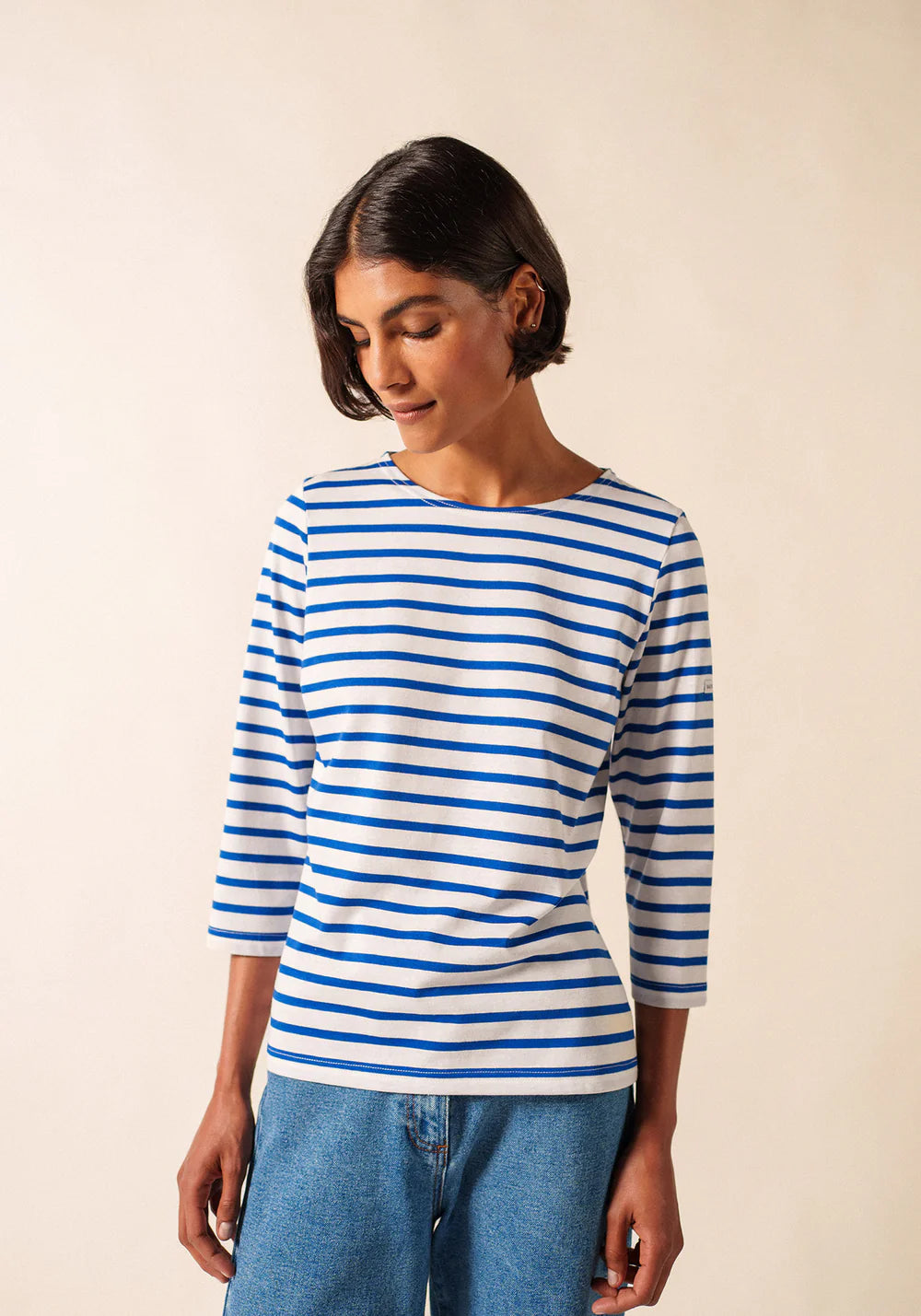 Eine Frau in einem SAINT JAMES Garde-Cote-Hemd und blauen Jeans steht da und schaut nach unten.