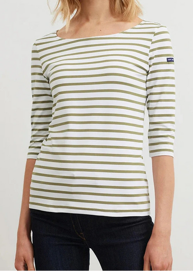 Frau in einem weißen SAINT JAMES Garde-Cote Marinière-Oberteil mit olivfarbenen Streifen und 3/4-Ärmeln, gepaart mit einer dunklen Hose.