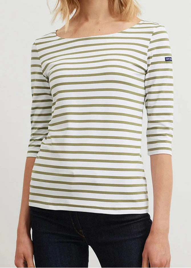 Frau in einem weißen SAINT JAMES Garde-Cote Marinière-Oberteil mit olivfarbenen Streifen und 3/4-Ärmeln, gepaart mit einer dunklen Hose.