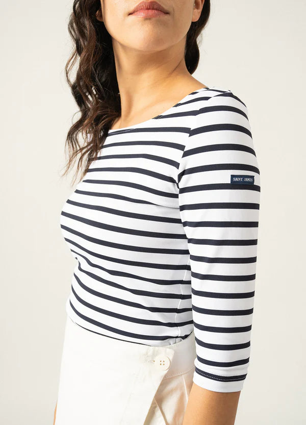 Frau in SAINT JAMES Garde-Cote, marineblaues und weißes Marinière-Oberteil mit Dreiviertelärmeln und weißem Rock, von der Seite gesehen.