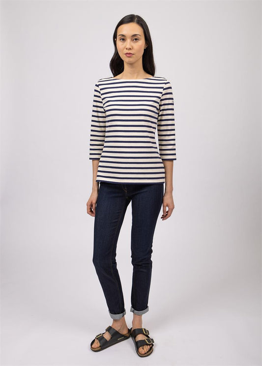 Frau im gestreiften SAINT JAMES Huitriere-Shirt, dunklen Jeans und Sandalen vor einem schlichten hellen Hintergrund.