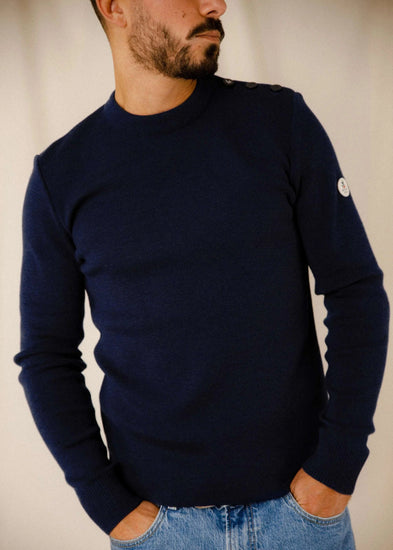 Mann trägt den ROYAL MER Klasel Pullover in Marineblau mit Rundhalsausschnitt und Knöpfen, gepaart mit Blue Jeans.