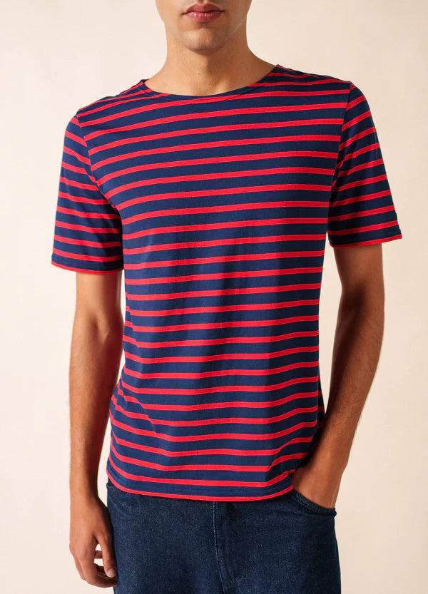 Eine Person trägt das marineblaue und rote SAINT JAMES Levant Marinière-T-Shirt mit blauer Hose, mit dem Gesicht nach vorne.